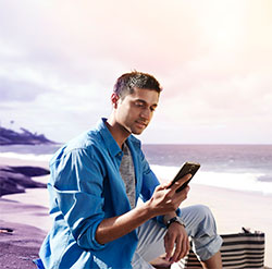 Man in blue shirt using speech recognition with his mobile device on the beach